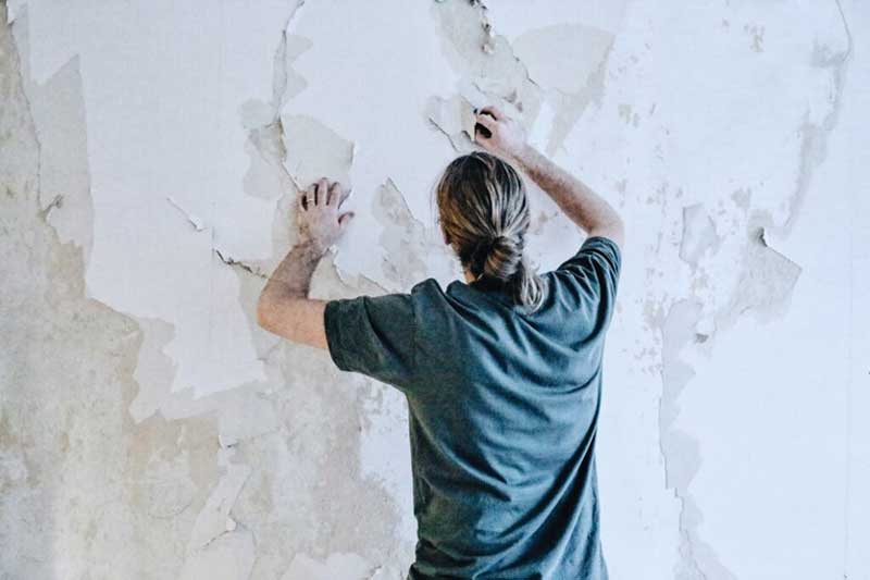A man peeling of the paint from a wall